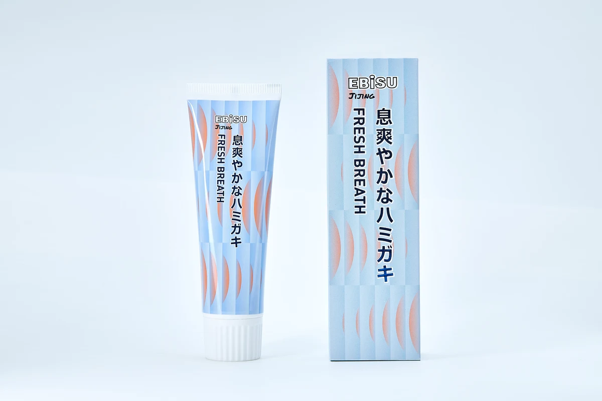 Japanese toothpaste tube beside its matching blue packaging on a clean pale background